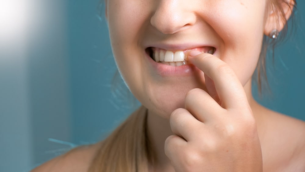 Une jeune femme tente de déprendre un morceau de nourriture coincé dans ses dents